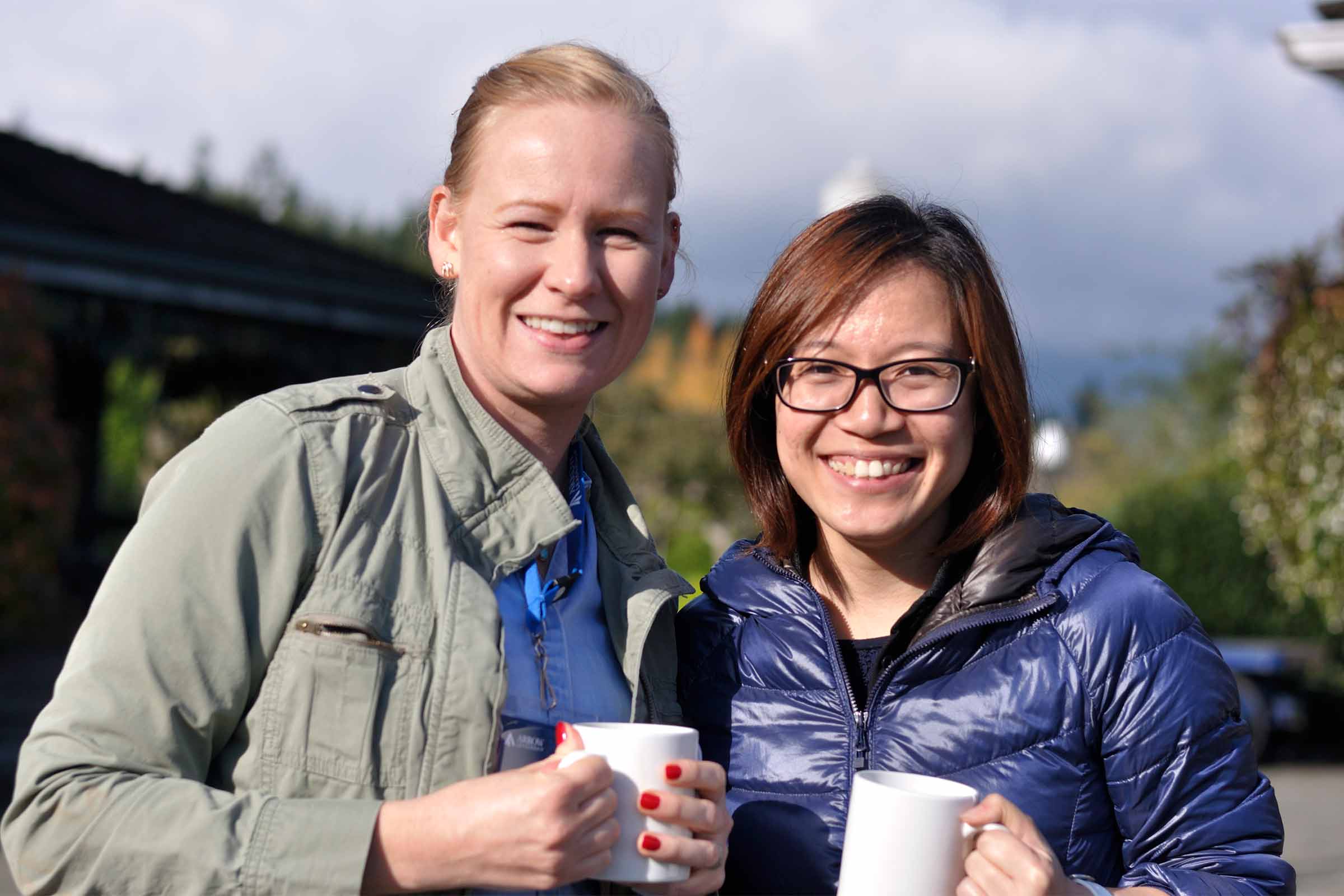 Two Women from Arrow Leadership Emerging stream smile while holding coffee